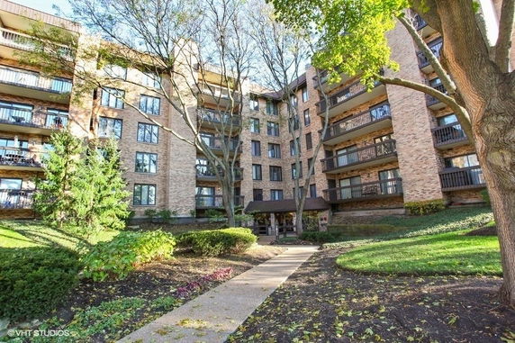 Front view of a multi-story residential building with balconies and a landscaped entrance.