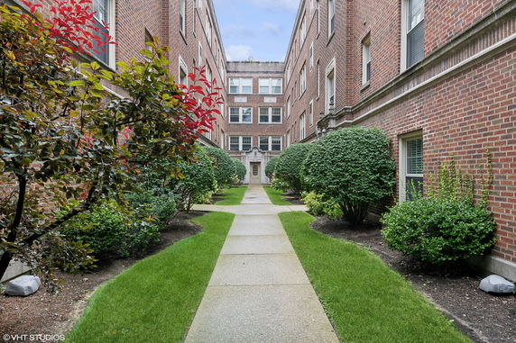 Front view of a brick apartment building with a pathway and greenery.
