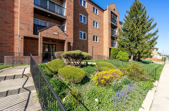 Front view of a multi-story brick building with balconies and landscaped garden.