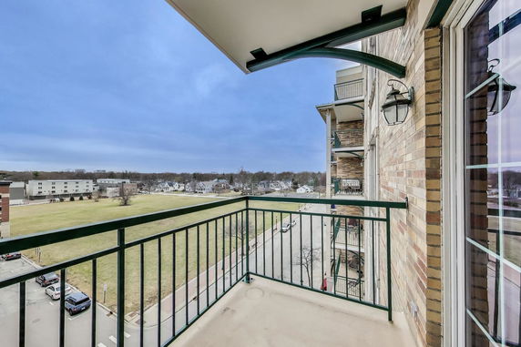 View from a balcony overlooking an open field and distant buildings.