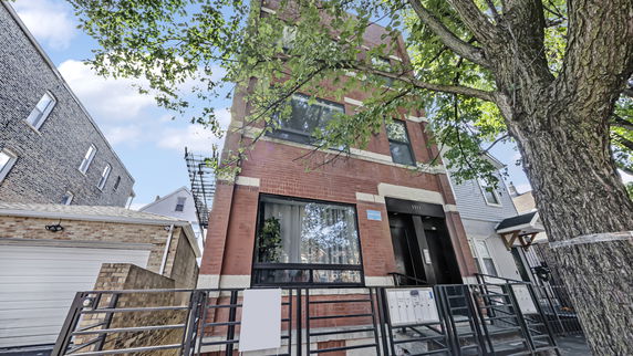 Front view of a multi-story brick building with windows and a tree in the foreground.