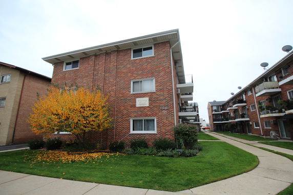 Front view of a three-story brick apartment building with balconies.