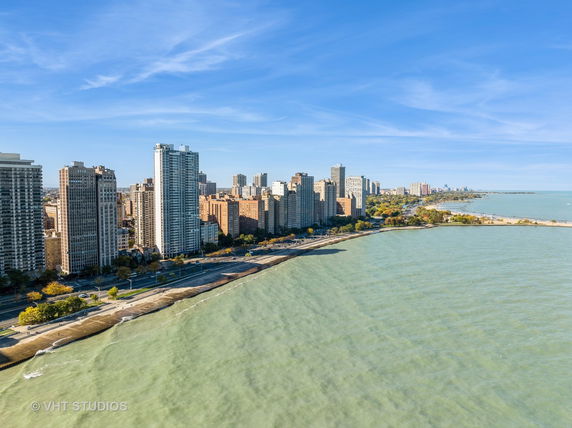 Panoramic view of a city skyline along a waterfront with tall buildings and a roadway.