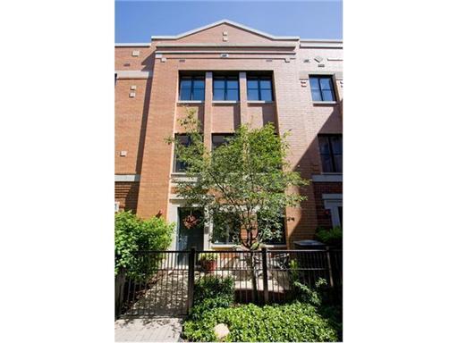 Front view of a multi-story brick townhouse with a small garden and gated entrance.