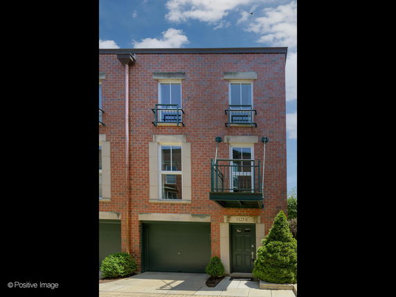 Front view of a brick townhouse with a garage and balcony.