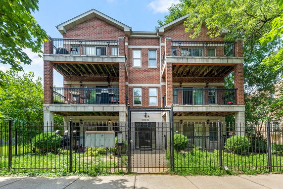 Front view of a multi-story brick building with balconies and a gated entrance.
