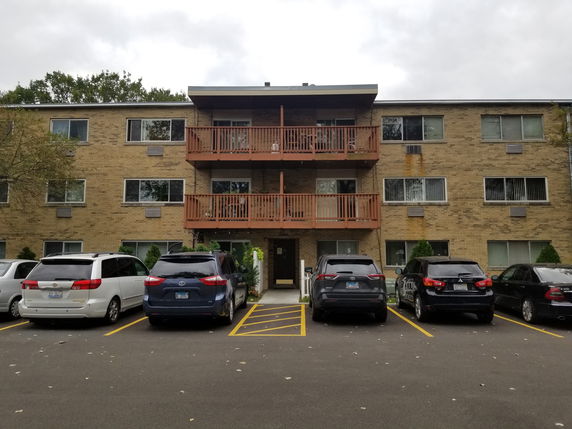 Front view of a multi-story apartment building with balconies and parking in front.
