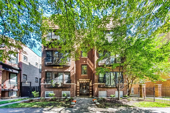 Front view of a multi-story brick apartment building with balconies and a central entrance.