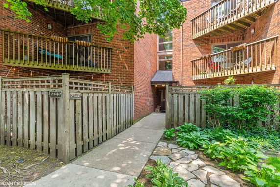 Front view of a brick apartment building with wooden balconies and a fenced entrance.