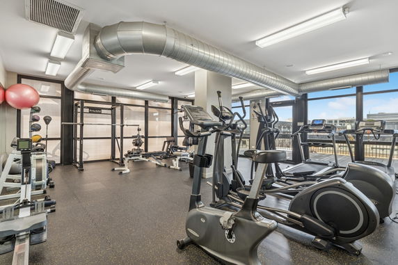 Interior view of a gym with various exercise equipment including treadmills, exercise bikes, and weight machines.