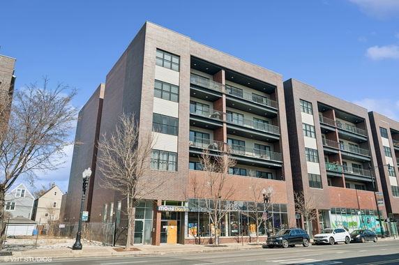 Front view of a multi-story apartment building with balconies and commercial spaces on the ground floor.
