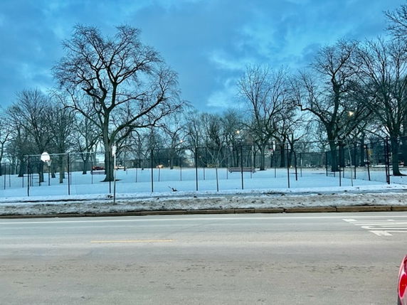 Snow-covered outdoor basketball court with trees around.