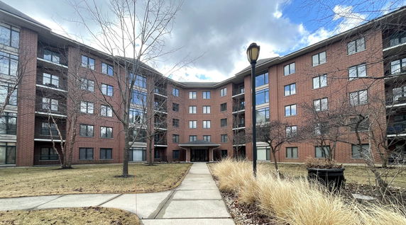Front view of a multi-story brick apartment building with multiple windows and an entrance canopy.