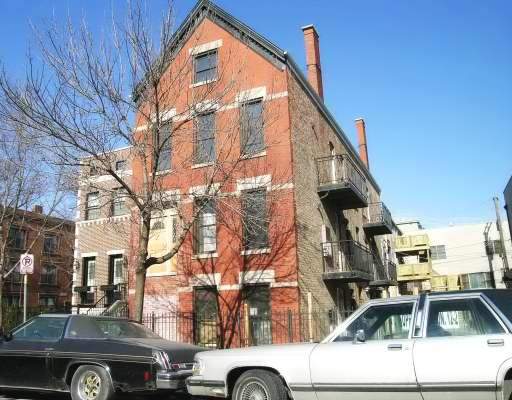 Front view of a three-story brick building with visible balconies and multiple chimneys.