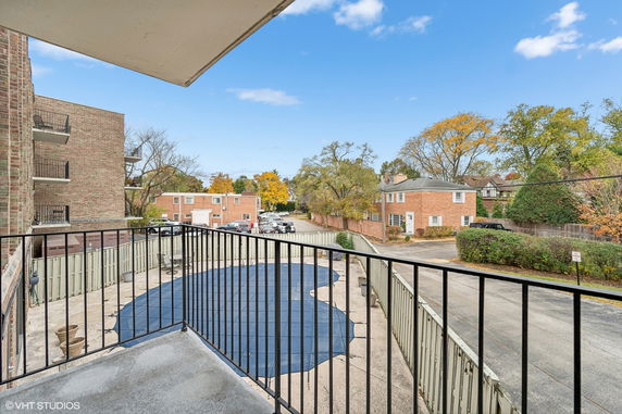 View from a balcony overlooking a small courtyard with covered pool and parking area, surrounded by brick buildings and trees.