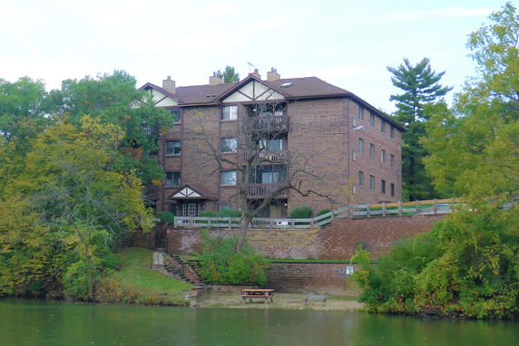 Front view of a multi-story brick building with balconies and a sloped lawn leading to a body of water.