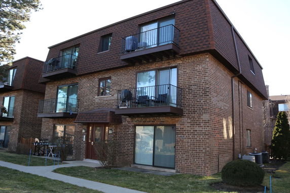 Front view of a three-story brick apartment building with balconies.