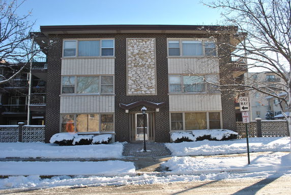Front view of a three-story apartment building with brick facade and large windows.