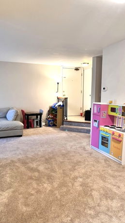Room with carpeted floor, sofa, toy kitchen, and children's play area.