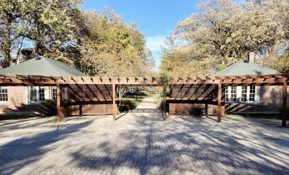 Front view of a brick building with wooden pergola structures, surrounded by trees.