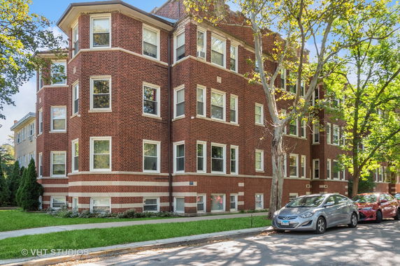 Front view of a multi-story red brick building with multiple windows and a sidewalk.