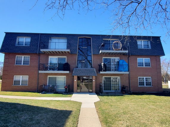 Front view of a three-story brick apartment building with balconies.