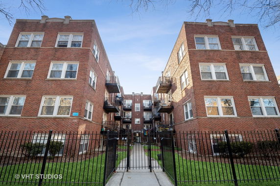 Front view of a brick apartment building with multiple balconies and a gated entry.