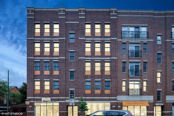 Front view of a multi-story brick building with shops at the ground level.