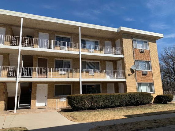 Front view of a three-story apartment building with balconies and brick exterior.