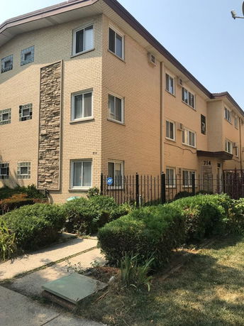 Front view of a three-story apartment building with beige brick exterior and decorative stone accents.