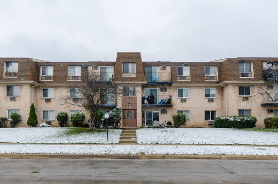 Front view of a three-story apartment building with a snowy lawn.
