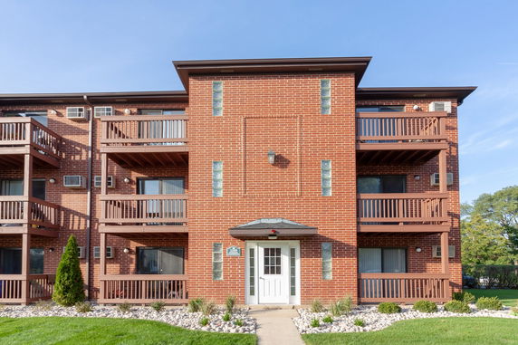 Front view of a three-story brick apartment building with balconies.
