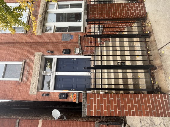 Front view of a brick building with stairs and a black metal gate.