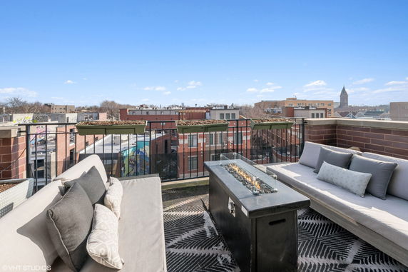 Rooftop seating area with a fireplace overlooking urban buildings.