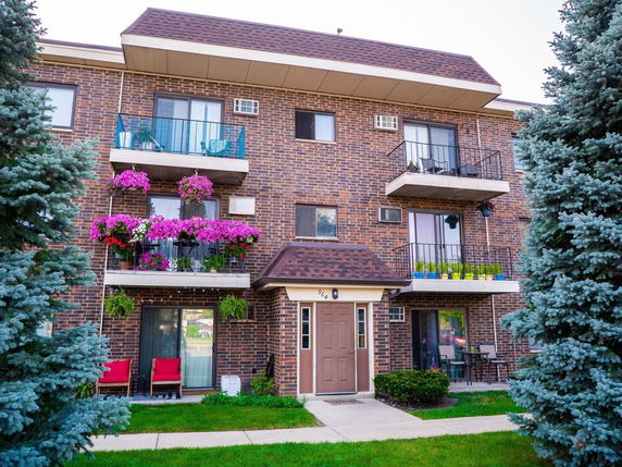 Front view of a multi-story brick apartment building with balconies and a main entrance.