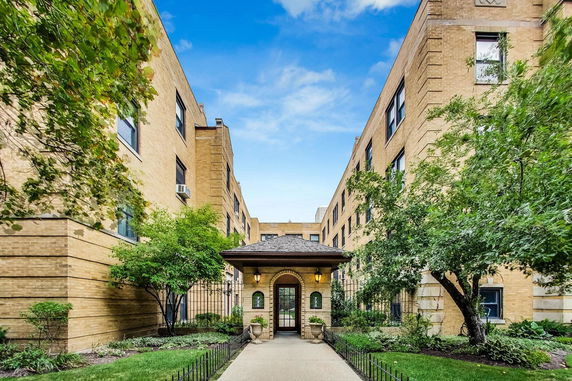 Front view of a multi-story brick apartment building with a central entrance and garden area.
