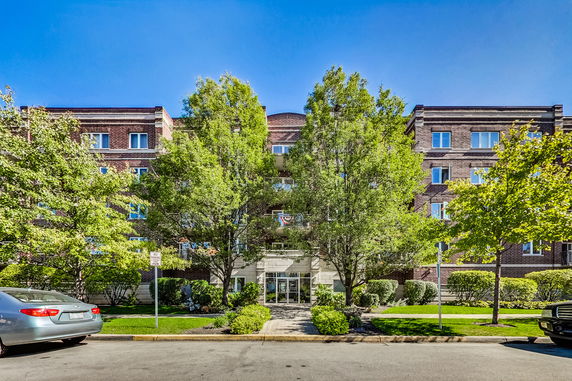 Front view of a multi-story brick apartment building with trees and cars in front.