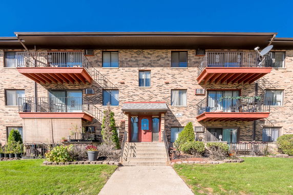 Front view of a three-story apartment building with balconies and brick facade.