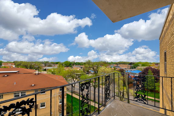 View from a balcony showing a wide-angle perspective of the surrounding neighborhood with rooftops and trees.