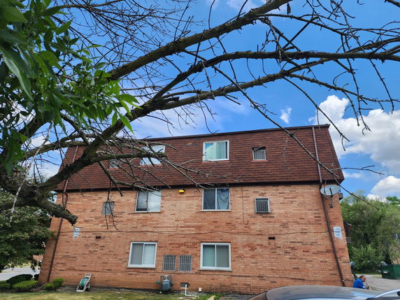 Front view of a multi-story brick building with a sloped roof and multiple windows.