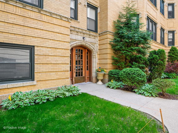 Front view of a brick building entrance with decorative plants and shrubs.