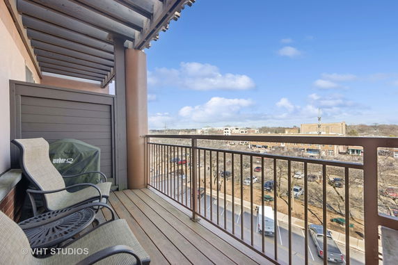 View from a balcony with two chairs and a grill, overlooking a parking area and surrounding buildings.