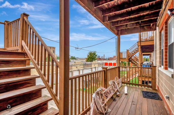 View from the wooden balcony of a building, showing nearby structures and a blue sky.