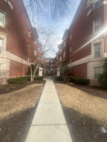 Front view of a multi-story red brick building with a paved walkway leading to the entrance.
