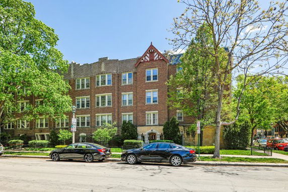 Front view of a multi-story brick apartment building with parked cars in front.