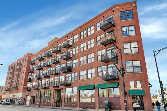 Front view of a multi-story brick building with balconies and ground-floor storefronts.