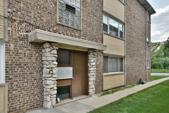 Front view of a multi-story brick building entrance with mailboxes and stone accents.