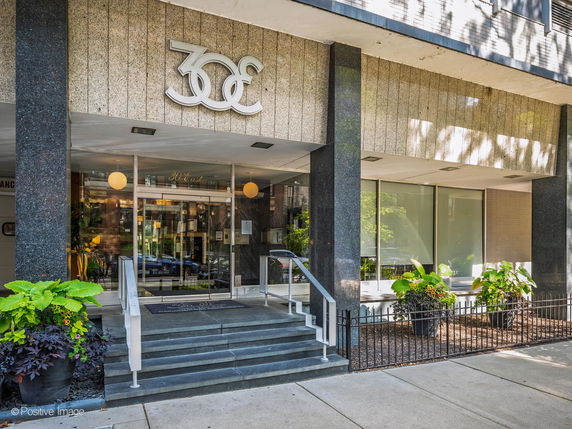 Front view of a building entrance with large glass doors and potted plants on the exterior steps.