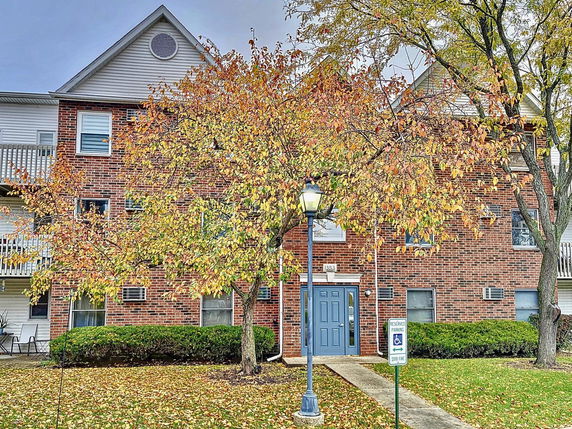 Front view of a brick multi-story building with a blue entrance door and autumn trees in front.