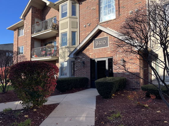 Front view of a multi-story brick building with balconies and entryway.